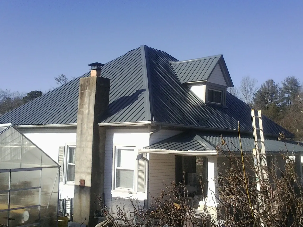 Dark blue standing seam metal roof on a white farmhouse with dormer — Slate & Tile Roof Repair by Roofing Brothers in East Lynn