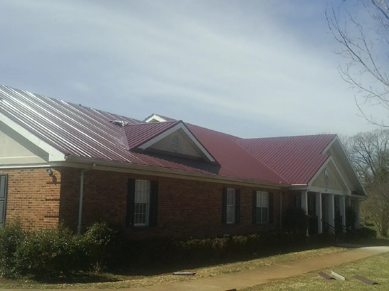 Red metal roof with gabled entries on a long brick building, from a Hail Damage Roof Repair job in East Lynn