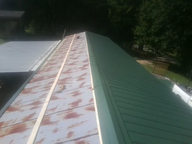 Old rusted panels beside newly installed green metal roofing — Wind Damage Roof Repair by Roofing Brothers in East Lynn