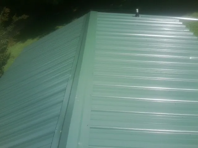 New green metal panels meeting at the ridge of a roof — Flat Roof Repair work by our crew in East Lynn
