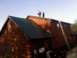 Crew on the ridge of a green metal roof on a two story log home in East Lynn