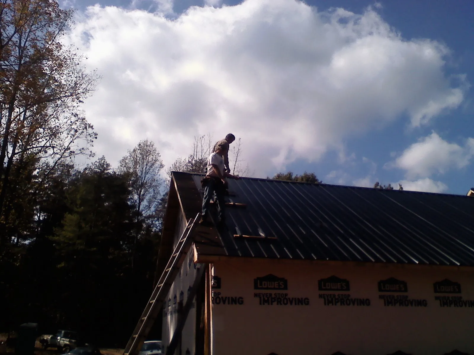 Roofer fastening dark metal panels high against a cloudy sky, from a Roof Inspection job in East Lynn