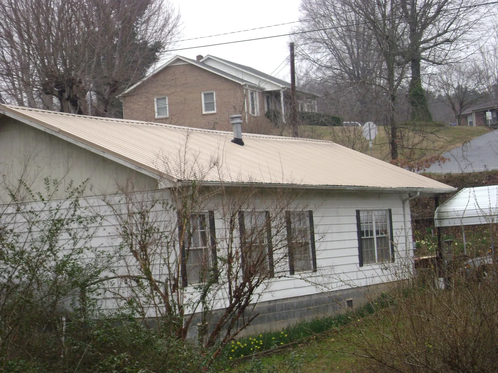 Tan metal roof on a white sided house set into a hillside — Commercial Roofing by Roofing Brothers in East Lynn